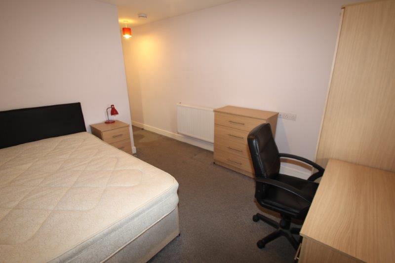 Student bedroom with double bed, chest of drawers, desk with black office chair and bedside table with red lamp