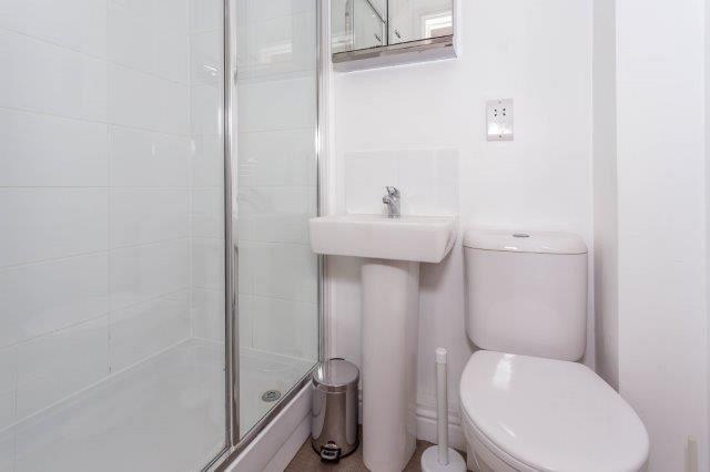 White student bathroom with shower and mirrored cupboard above sink