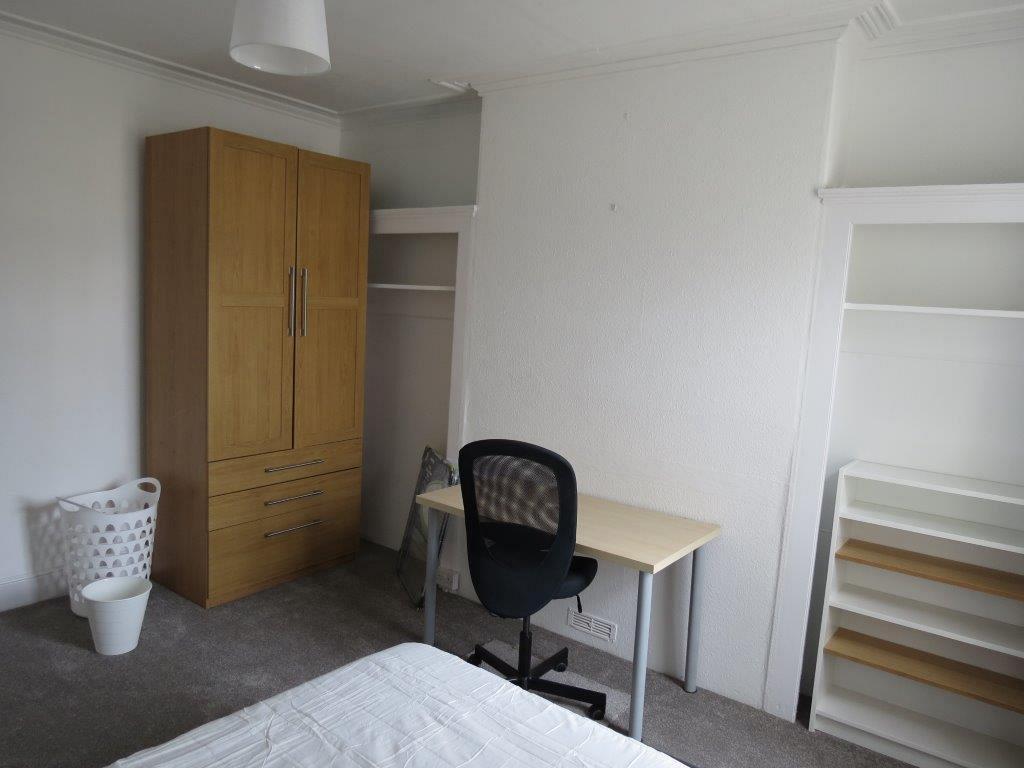 student bedroom with double bed, two door wardrobe, shelving unit and desk with black office chair
