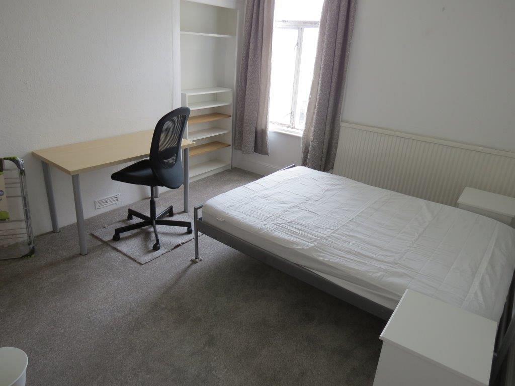 student bedroom with double bed, shelving unit, desk with black office chair and white bedside table
