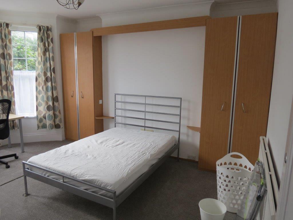student bedroom with double bed, desk with black office chair in front of large bay windows and two two door wardrobes, 