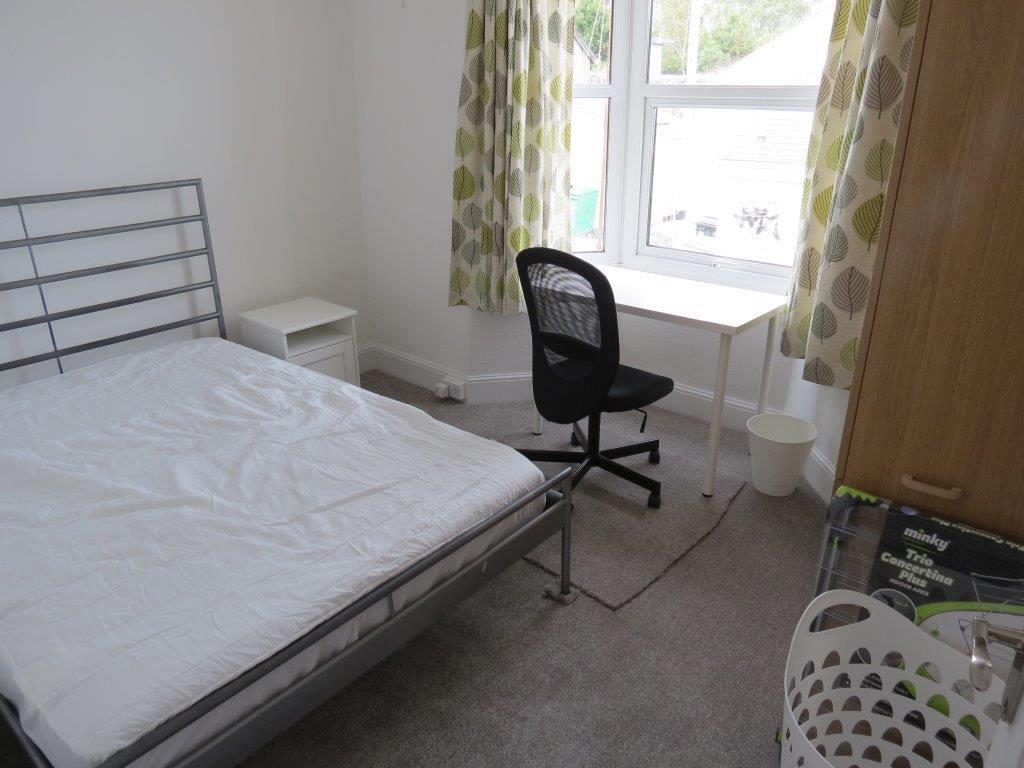 student bedroom with double bed, bedside table, desk with black office chair in front of window and two door wardrobe