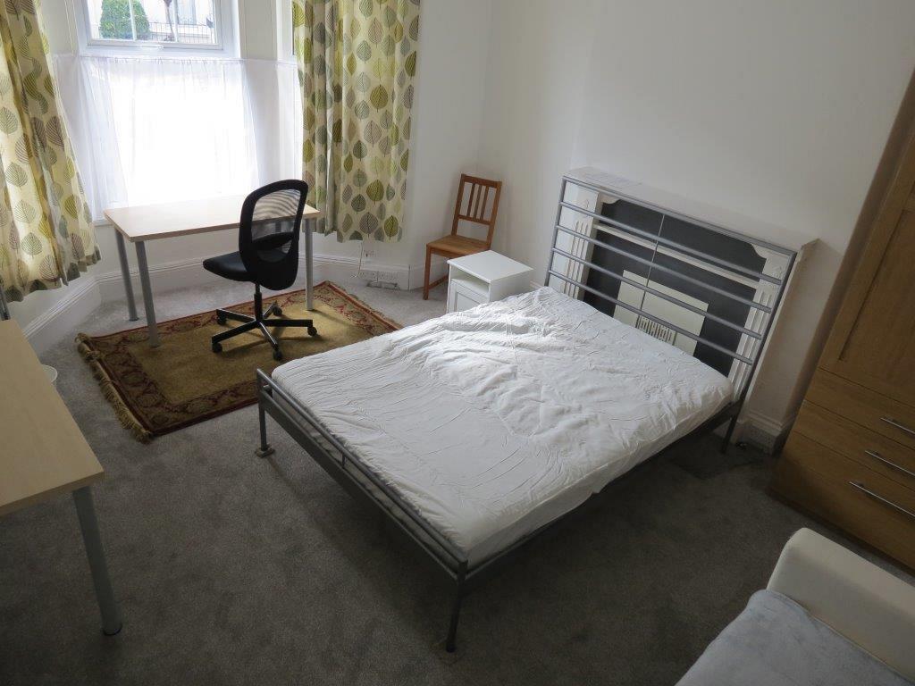 student bedroom with double bed, bedside table, desk with black office chair and two door wardrobe with drawers underneath