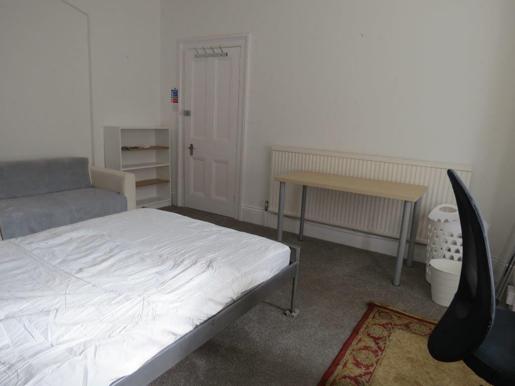 student bedroom with double bed, desk with black office chair, shelving unit and two-seater sofa