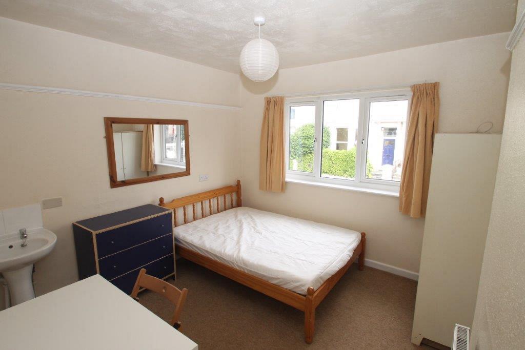First student bedroom with double bed, white two door wardrobe, chest of drawers, sink and desk with chair