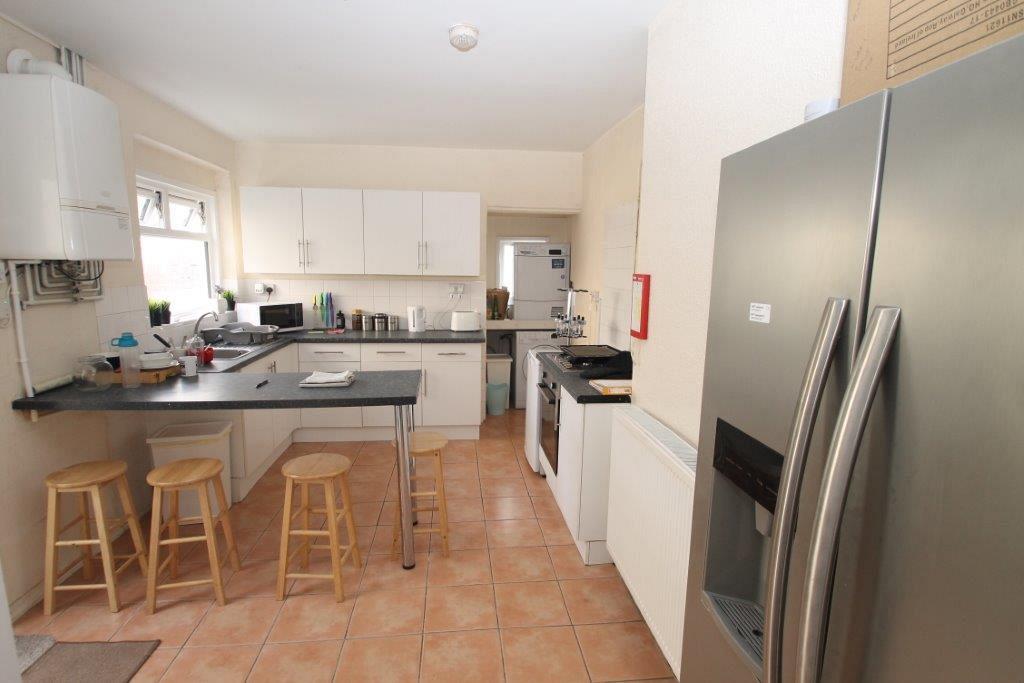 Shared kitchen with two door fridge freezer, small breakfast bar with four wooden bar stools, electric hobs and cooker, washing machine and isnk