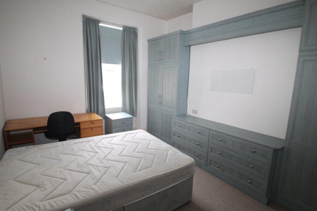 first student bedroom with double bed, desk with black office chair, bedside table, x2 two door wardrobes, two large grey chest of drawers