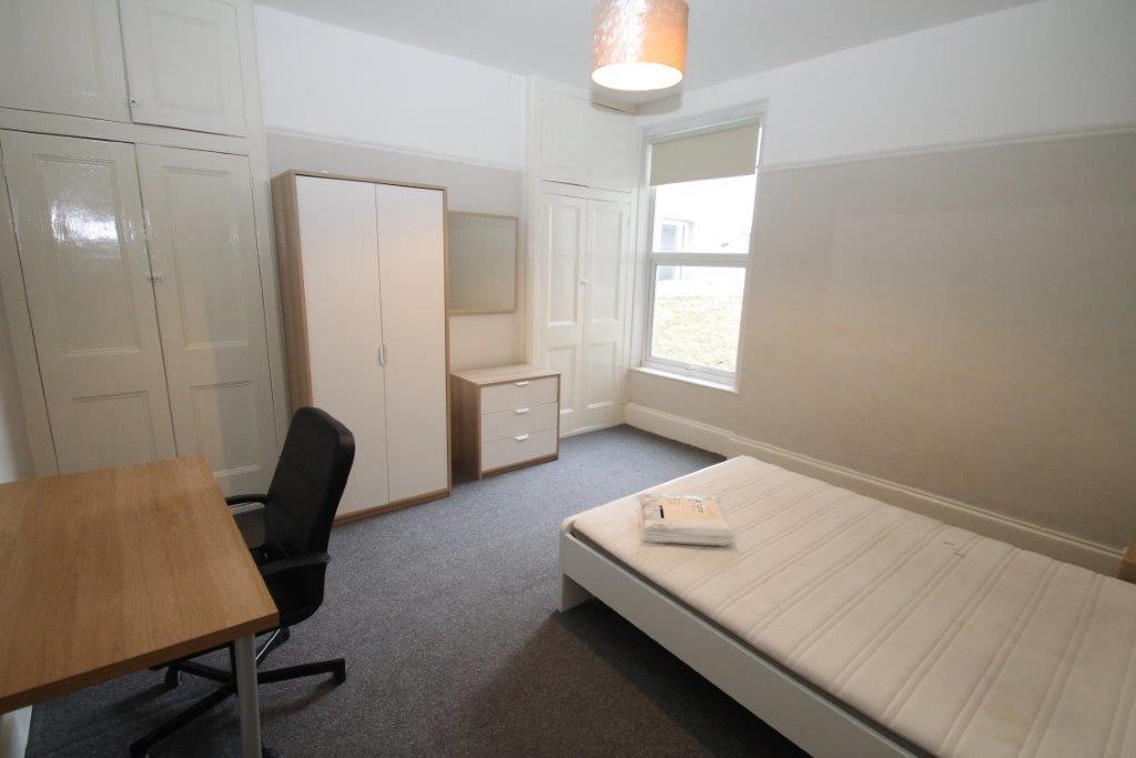 Second student bedroom with double bed, two door wardrobe, chest of drawers, desk with black office chair and two built-in storage wardrobes