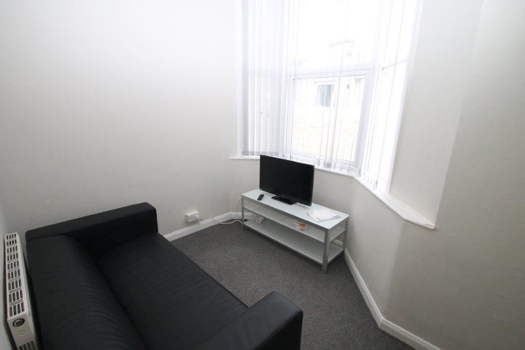 Living area with black two-seater sofa, tv on tv stand and bay windows