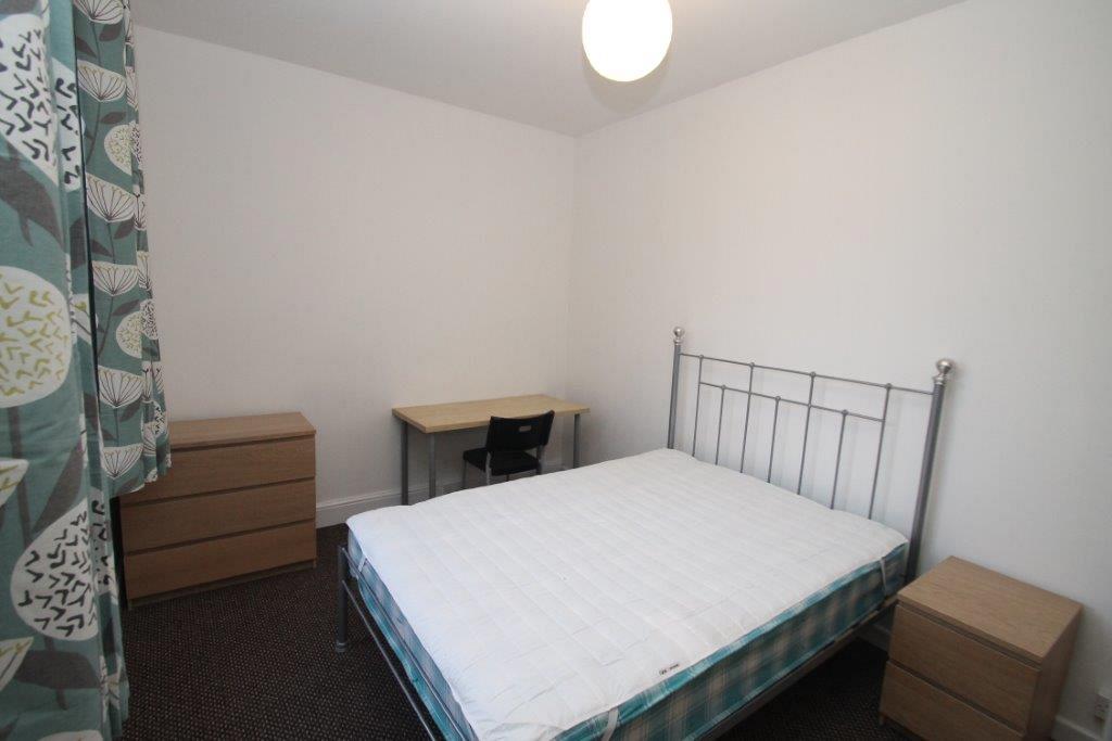 Student bedroom with double bed, desk with black chair, chest of drawers and bedside table