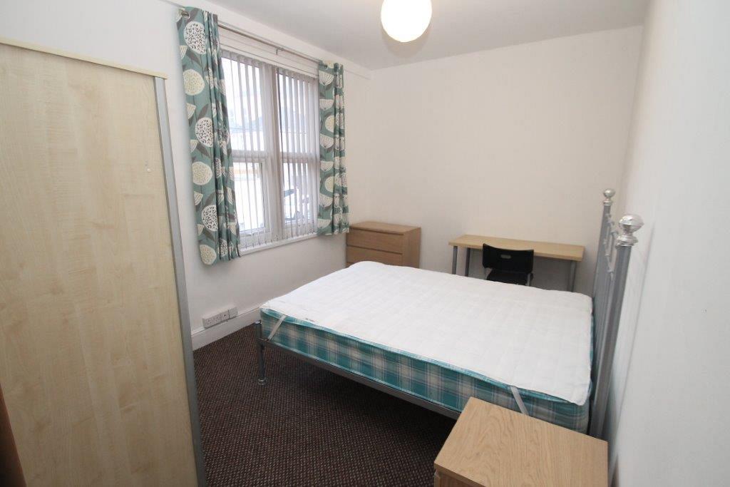 Student bedroom with double bed, two door wardrobe, chest of drawers and desk with black chair