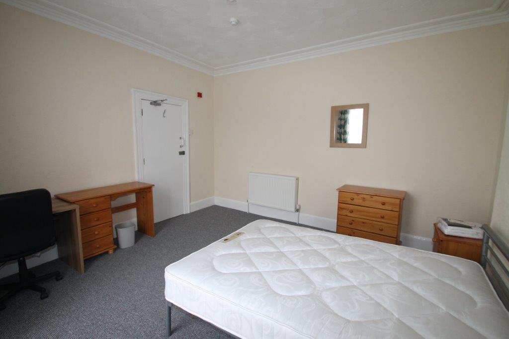 Sixth student bedroom with double bed, bedside table, two desks, chest of drawers and mirror mounted on wall
