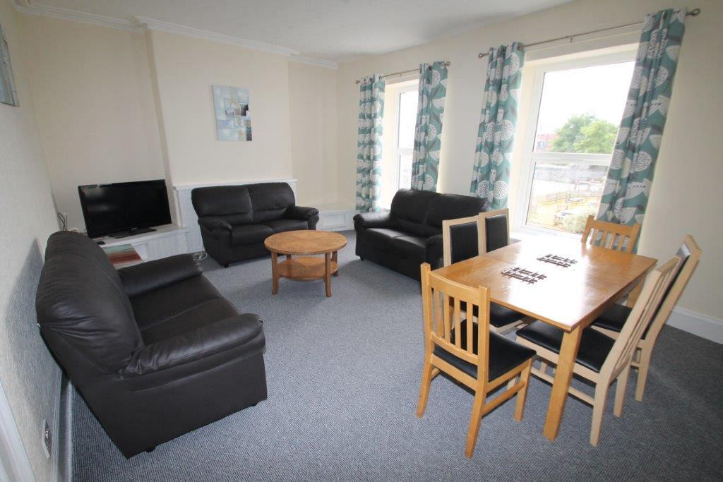 Shared living room with three black two-seater sofas, six-seater dining table and television