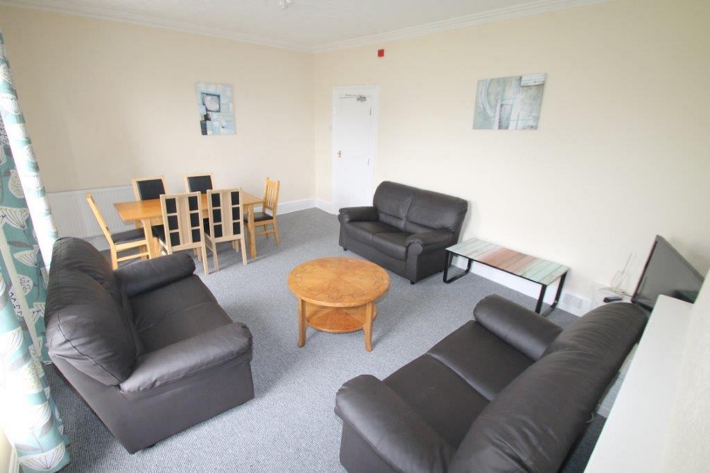 Shared living room with three black two-seater sofas, six-seater dining table and two coffee tables