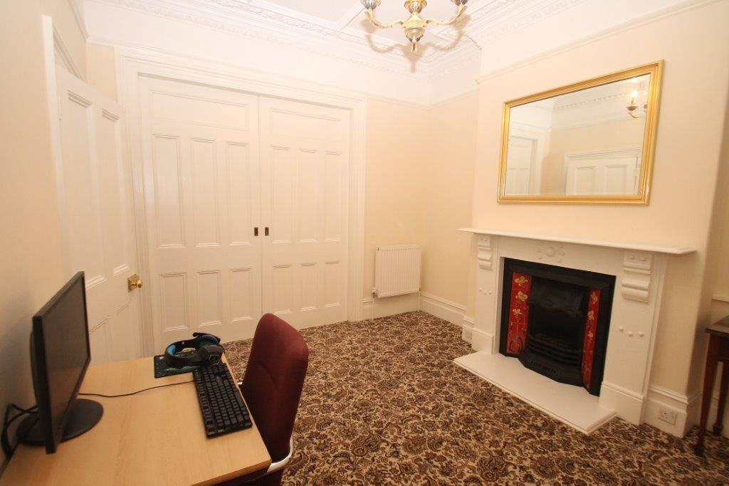 Room with white feature fire place, mirror on wall and desk photo taken from opposite corner