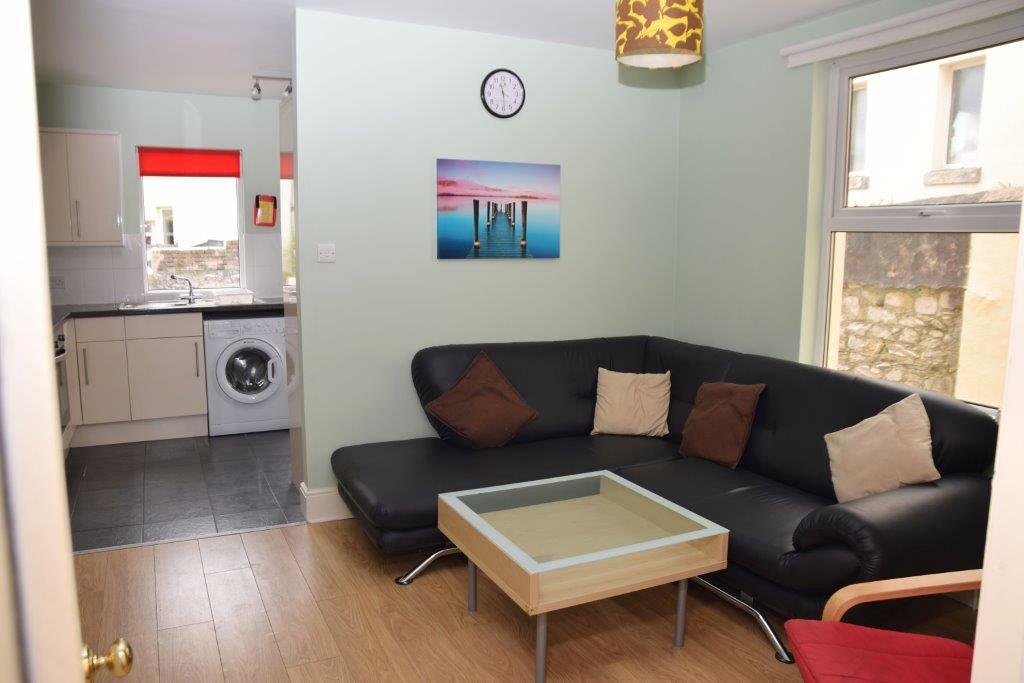 Shared living space with L shape sofa, red arm chair, leading into kitchen
