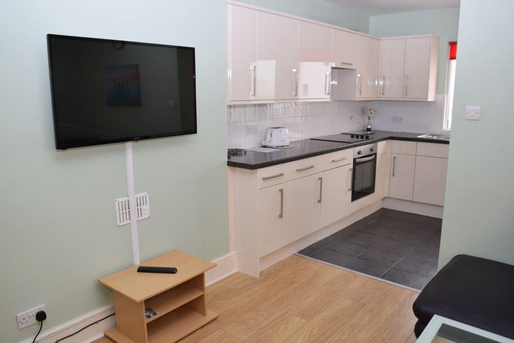 Shared living room with tv, leading into kitchen with induction hob and cooker