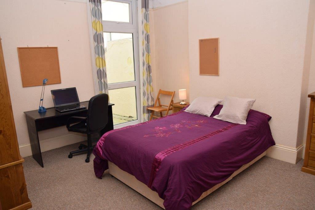 Second student bedroom with double bed, chest of drawers, three door wardrobe, desk and two pin boards on walls