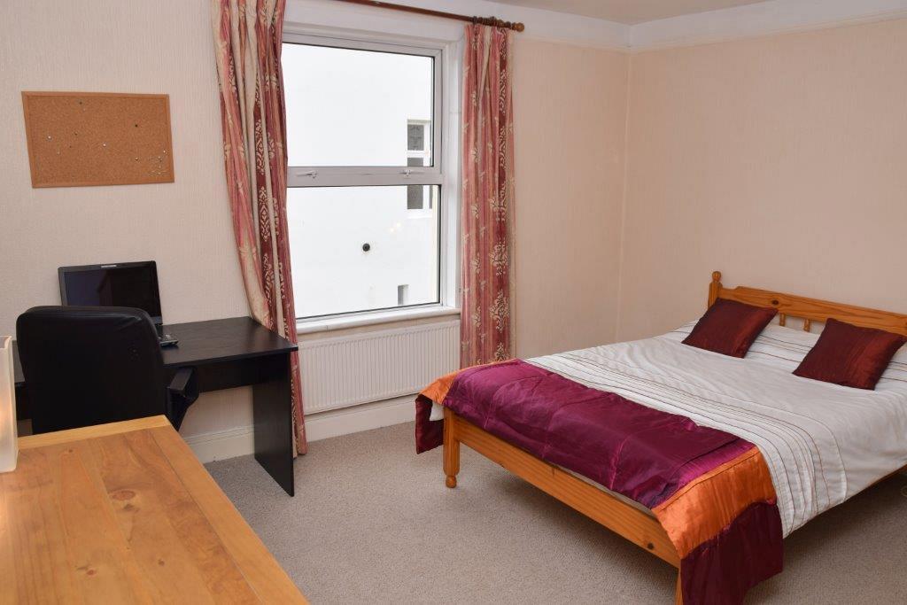 Third student bedroom with doubled bed, large window, black desk with pin board on wall