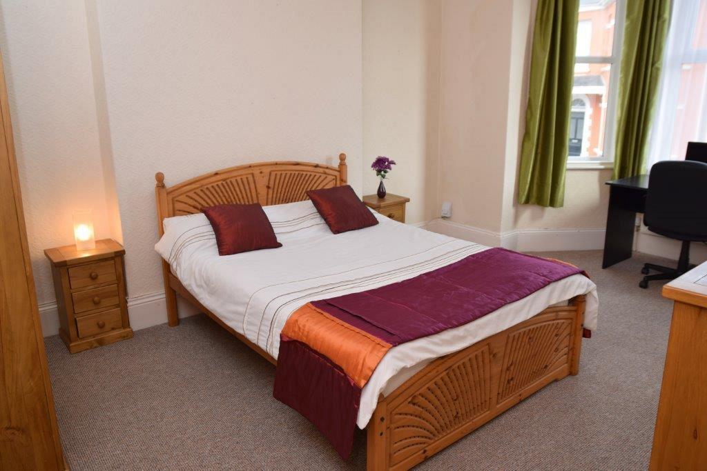 Fifth student bedroom with double bed, two bedside tables, chest of drawers and black desk in front of large bay windows