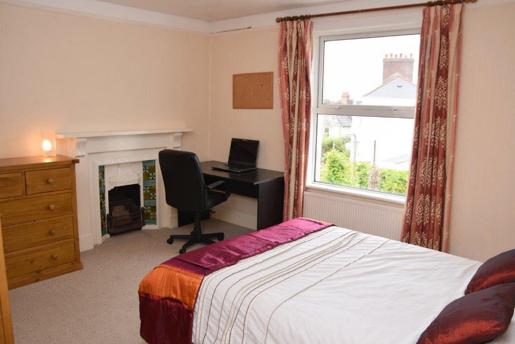 Third student bedroom with double bed, chest of drawers, large window, fireplace, desk and pin board on wall