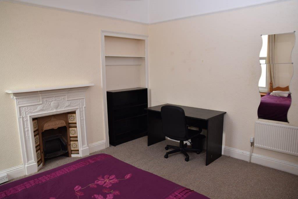 Fourth student bedroom with double bed, fire place, black shelving unit, black desk and full length mirror on wall