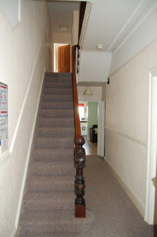 Hallway leading to shared living space and kitchen, with stairs leading upwards