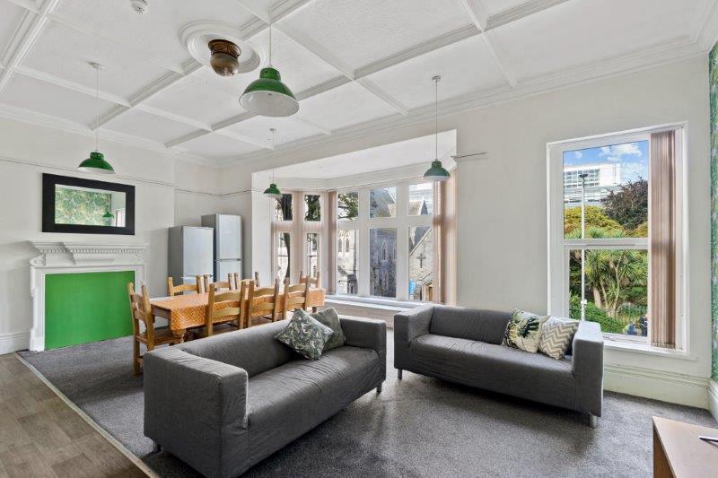 living space with two grey sofas, dining table with eight dining chairs, two fridge freezers and large bay windows