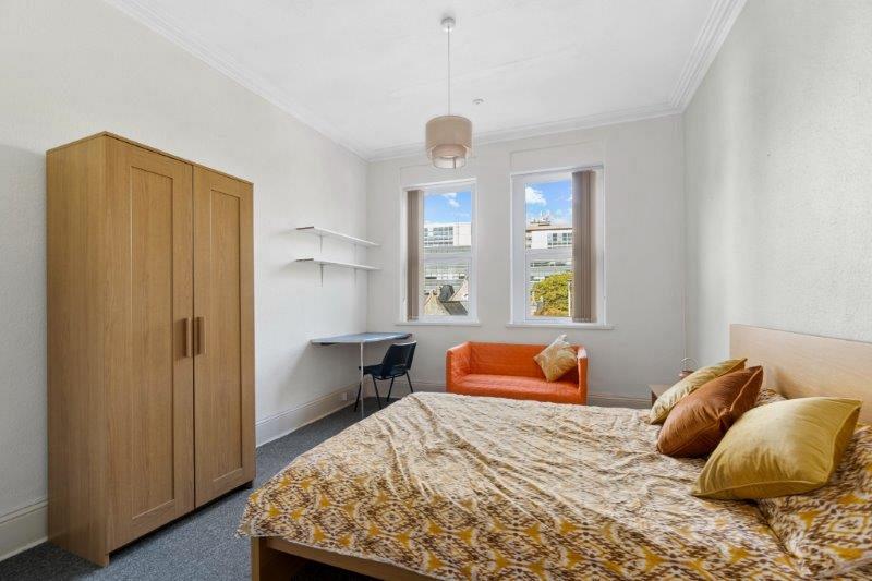 Student bedroom with double bed, two door wardrobe, desk, two shelves and two large windows