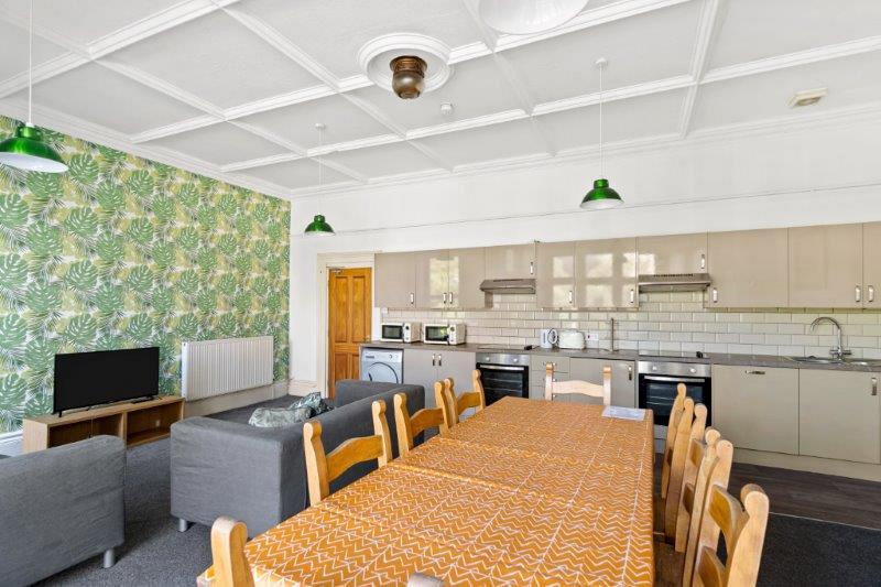 open plan kitchen and living area with dining table with eight dining chairs, two grey sofas, two cookers with induction hobs, washing machine, tumble dryer, dishwasher and two microwaves