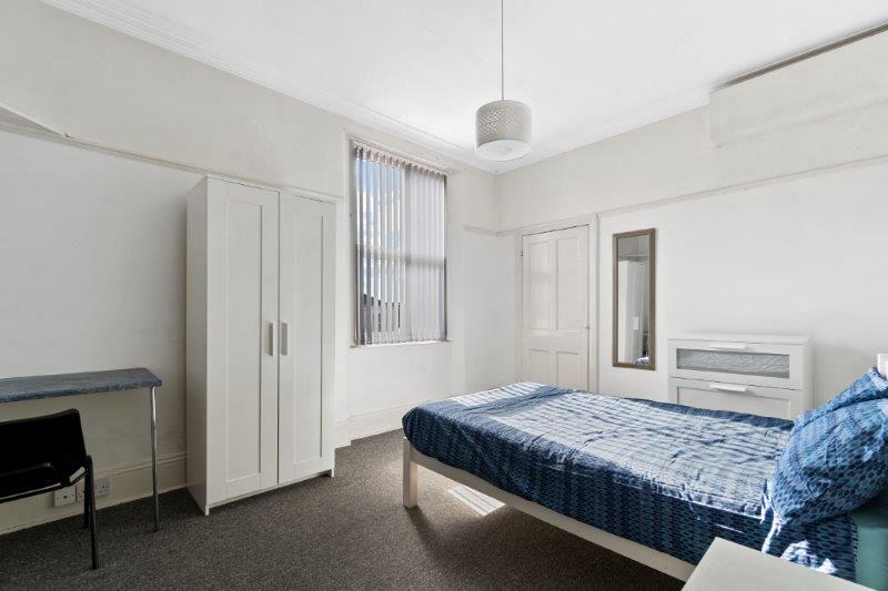 Student bedroom with double bed, chest of drawers, white two door wardrobe and desk with office chair