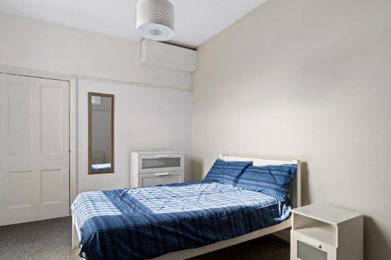 Student bedroom with double bed, chest of drawers, white bedside table and full length mirror