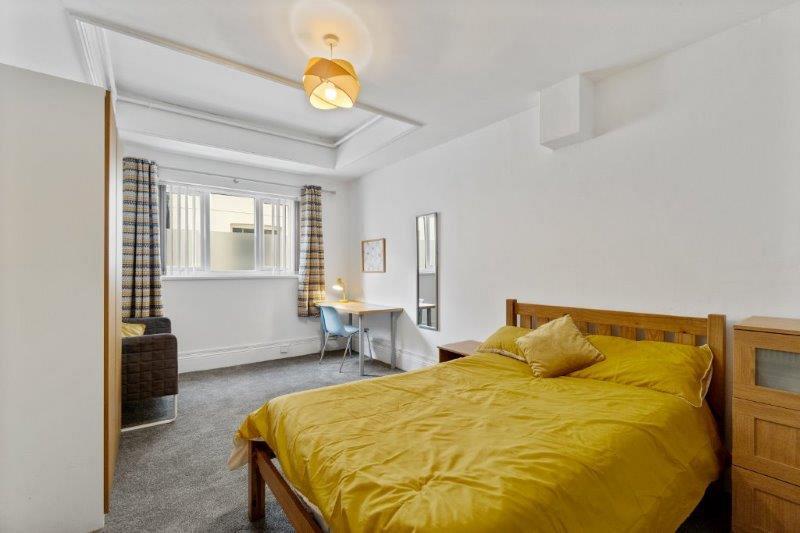 student bedroom with double bed, chest of drawers, two door wardrobe, grey armchair, full length mirror and desk with chair