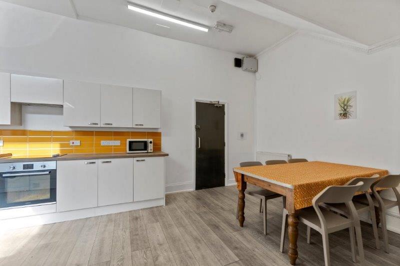 yellow tiled kitchen with two induction hobs and cooker, microwave and dining table with six dining chairs