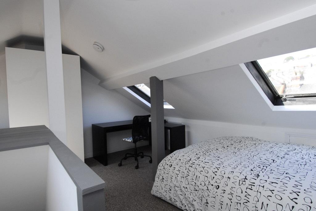 Fourth student attic bedroom with double bed, black L shaped desk with office chair, white two door wardrobe and two large skylight windows