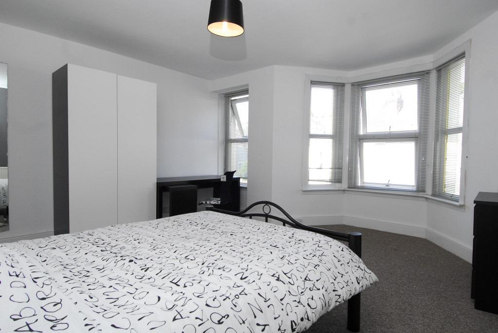 First student bedroom with double bed, black chest of drawers, black desk with office chair, white two door wardrobe and large bay windows