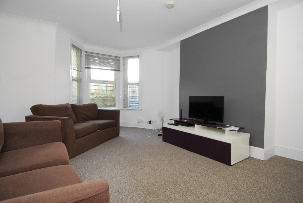 Spacious living area with two brown two-seater sofas, large bay windows, grey feature wall and tv on tv stand