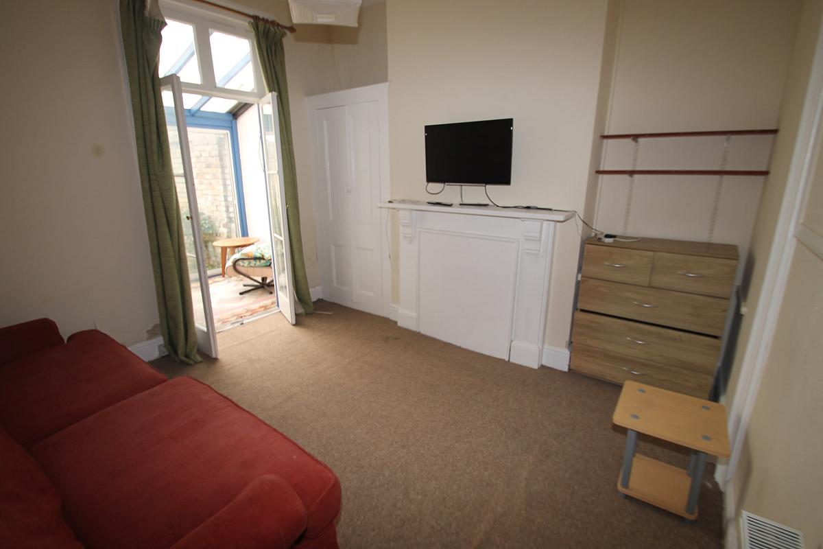 Shared living room with red two seater sofa, wall mounted tv, chest of drawers and leading into small conservatory