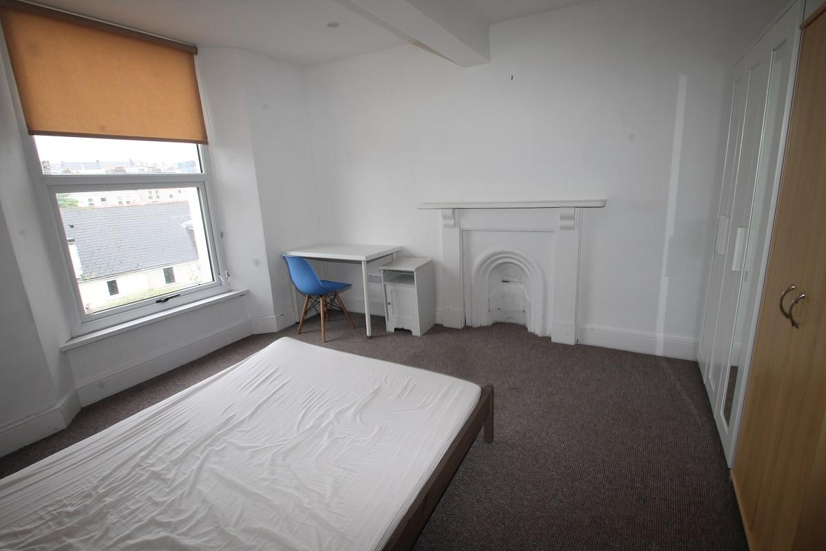 Student bedroom with double bed, white three door wardrobe with full length mirror, a wooden two door wardrobe, white desk with blue chair and large window