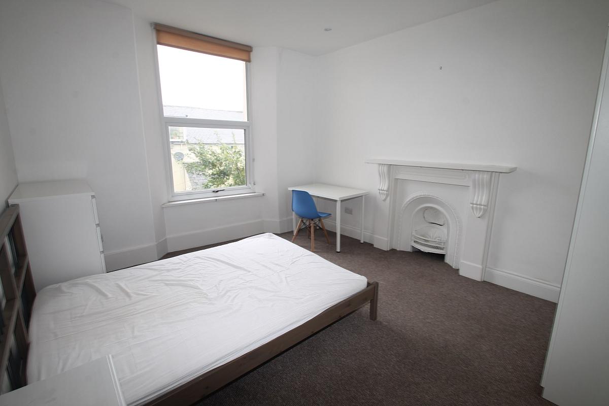 Student bedroom, double bed, white chest of drawers, white desk with blue chair and white feature fire place
