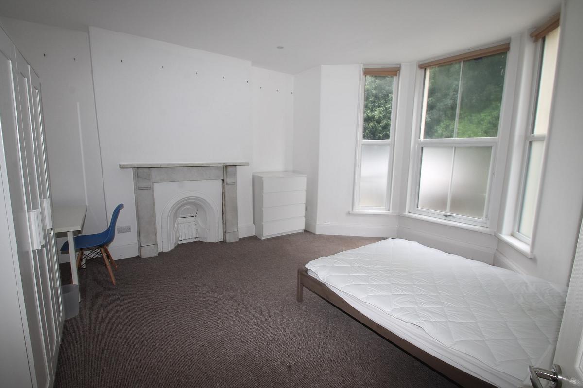 Student bedroom with double bed, white chest of drawers, three door wardrobe with full length mirror, white desk with blue chair and white feature fireplace