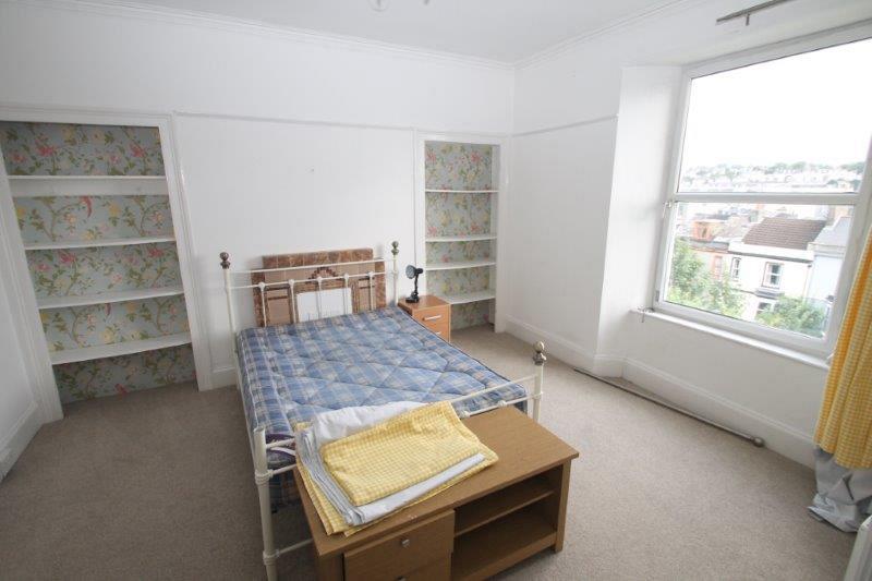Spacious student bedroom with double bed, large window, two built-in storage shelves and small chest of drawers at end of bed