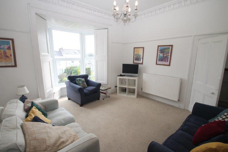 Shared living room with two double sofas, two armchairs, tv on white tv stand and large bay windows