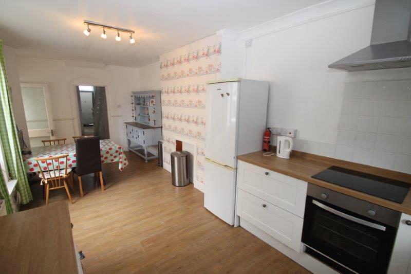 Shared kitchen with fridge freezer, induction hobs and cooker leading to dining table with four dining chairs#
