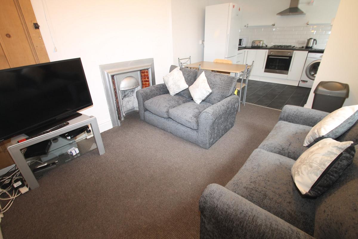 living space with two grey two-seater sofas, tv on tv stand and dining table with four dining chairs leading into kitchen
