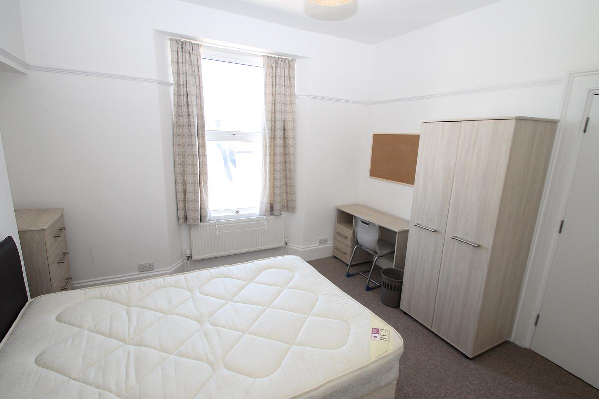 Third student room with double bed with two door cupboard, chest of drawers, shelving unit and desk