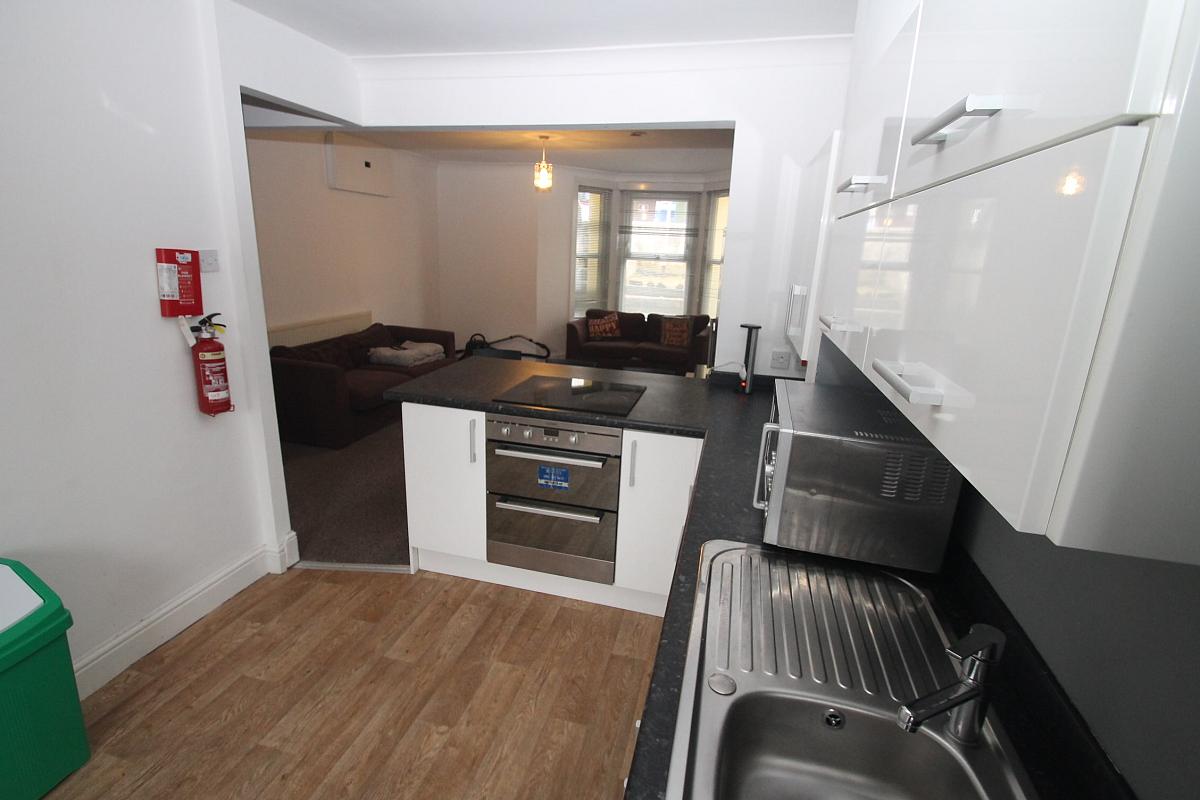 Shared kitchen with induction hobs and cooker, living area behind kitchen