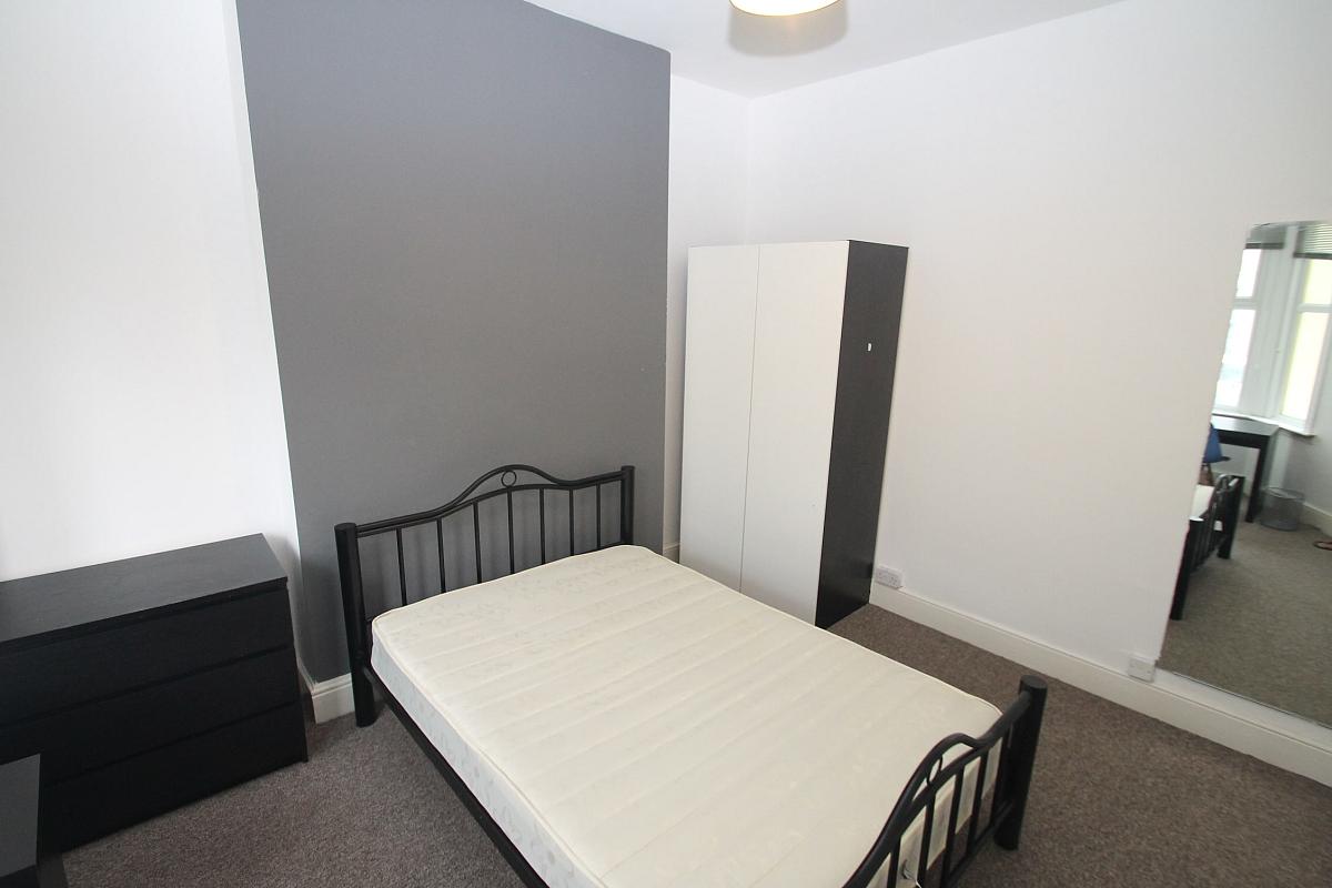 Second student bedroom with double bed, two door wardrobe, black chest of drawers, full length mirror and desk with chair in front of windows