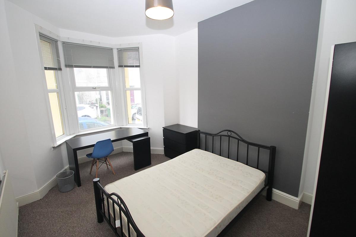 Second student bedroom with double bed, black chest of drawers, two door wardrobe and desk with blue chair in front of windows