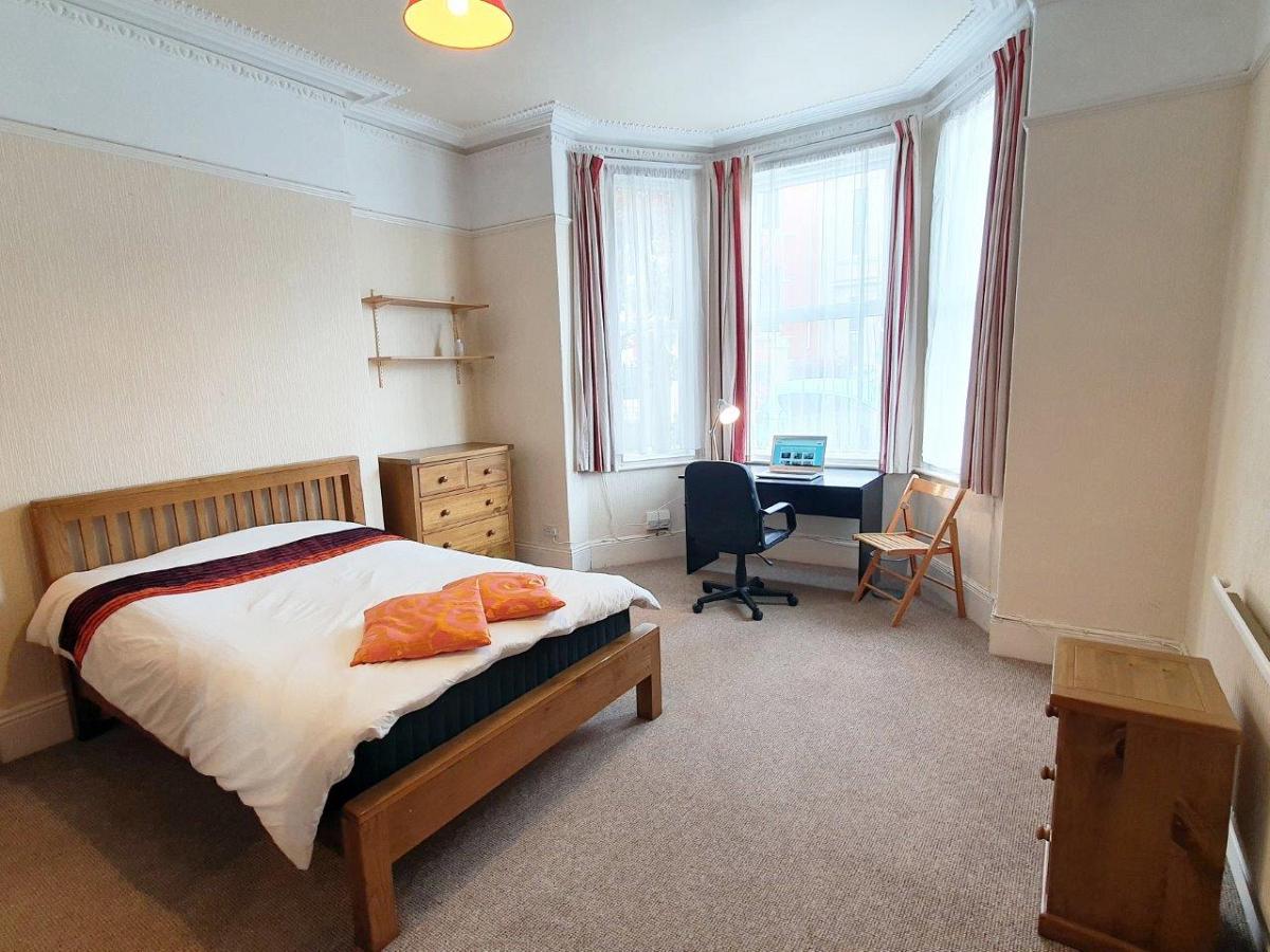 First student bedroom with double bed, chest of drawers, bedside table, two shelves and black desk in front of large bay windows
